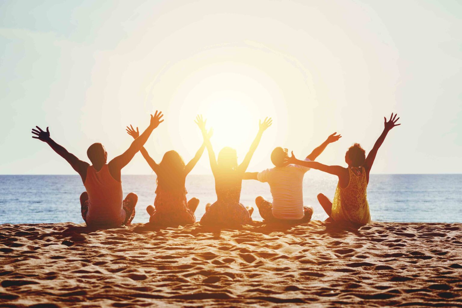 Five friends raising their arms on the sand at sunset in Myrtle Beach
