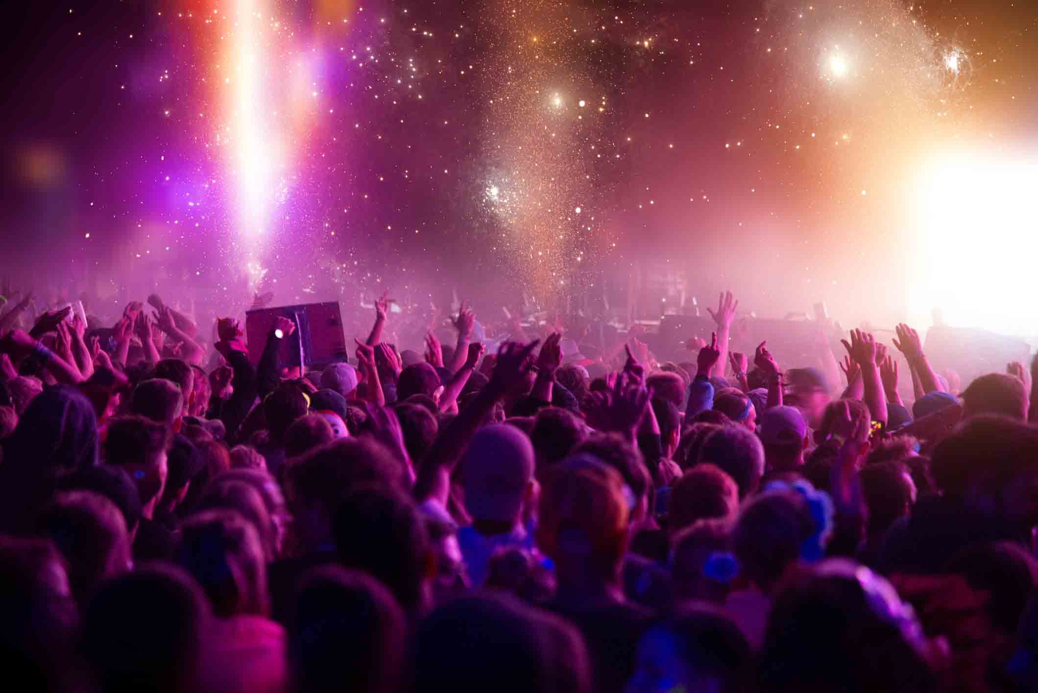 Concert crowd with hands raised under pink and purple stage lights