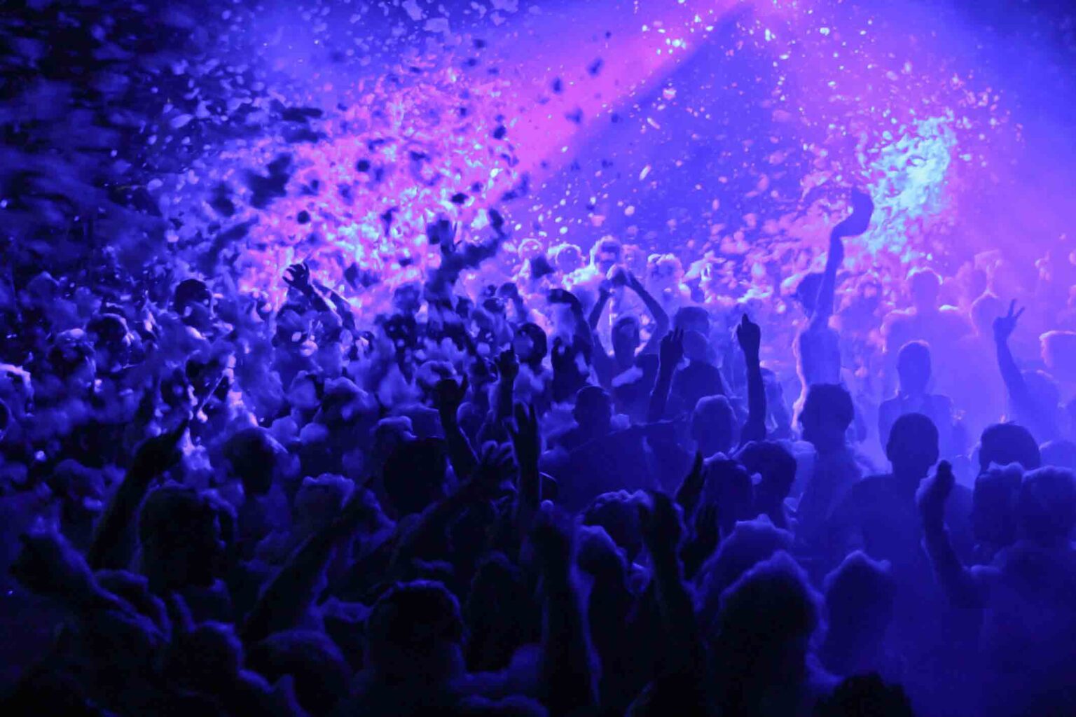 Crowd under blue lights and flying foam at a Senior Week foam party
