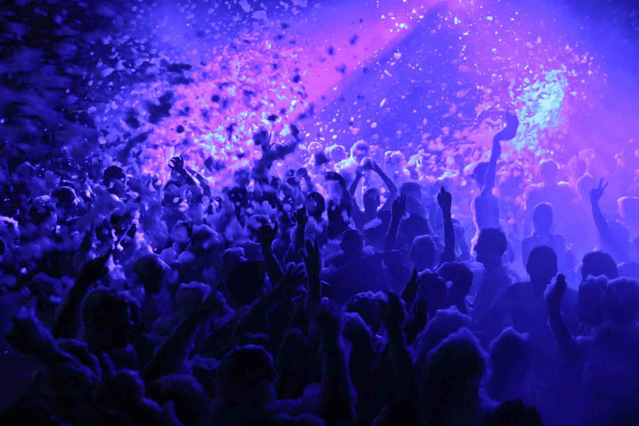 Crowd under blue lights and flying foam at a Senior Week foam party