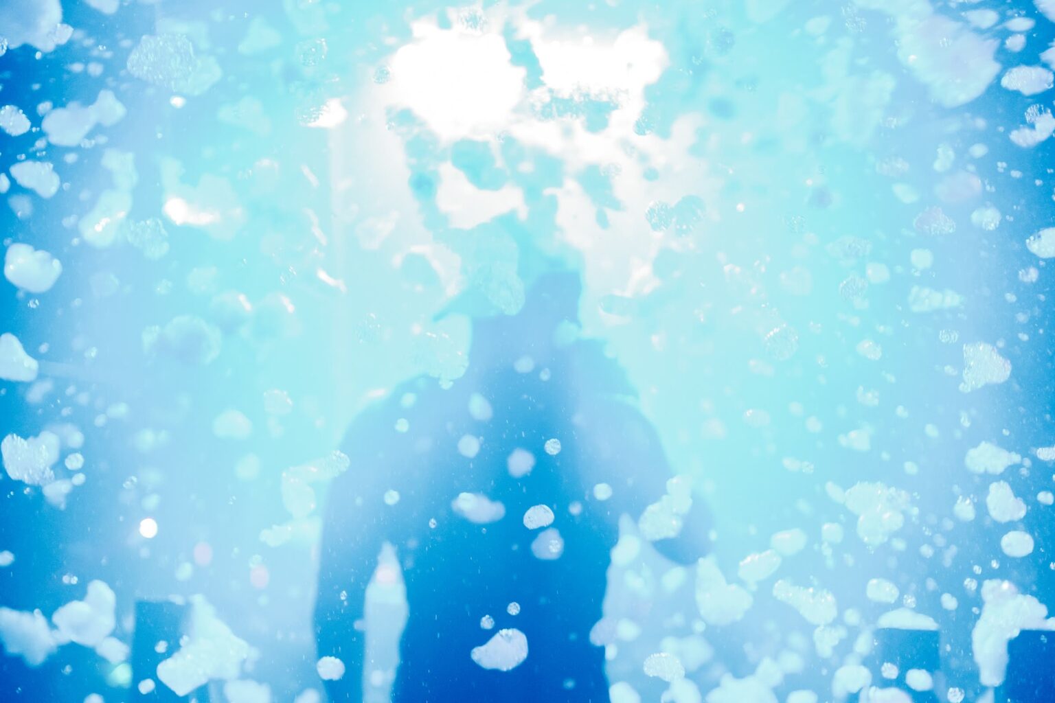 Silhouette on stage surrounded by flying foam under bright blue lights at a Senior Week foam party