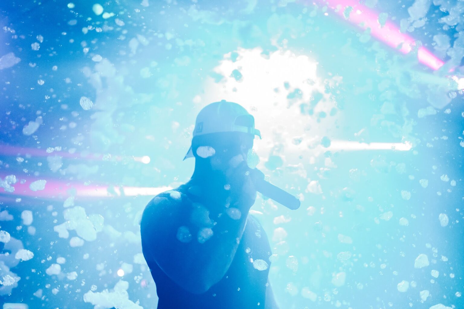 Performer with a microphone on stage in a cloud of foam at a Senior Week foam party