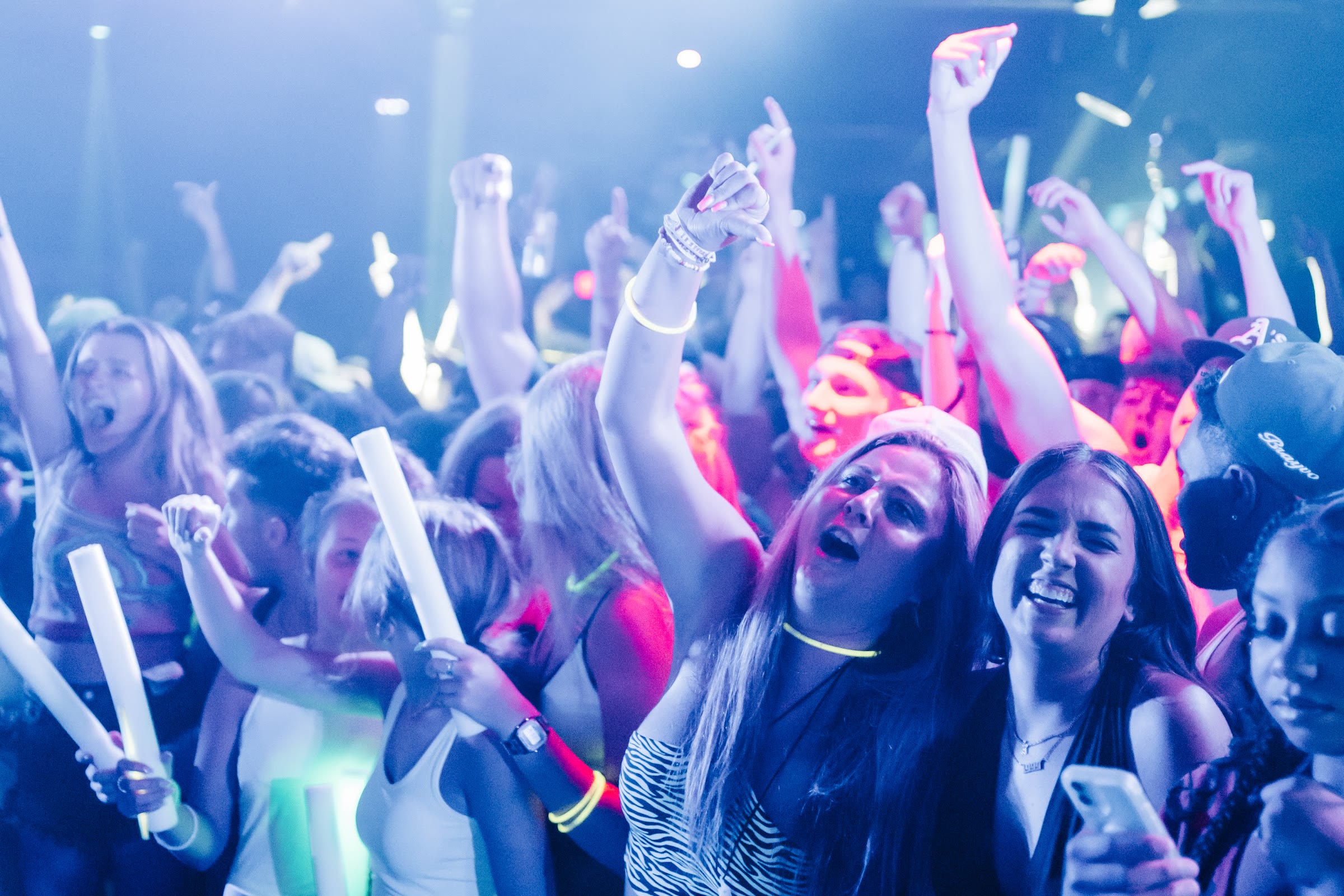 Grads cheering with glow sticks and neon bracelets at a Senior Week glow party