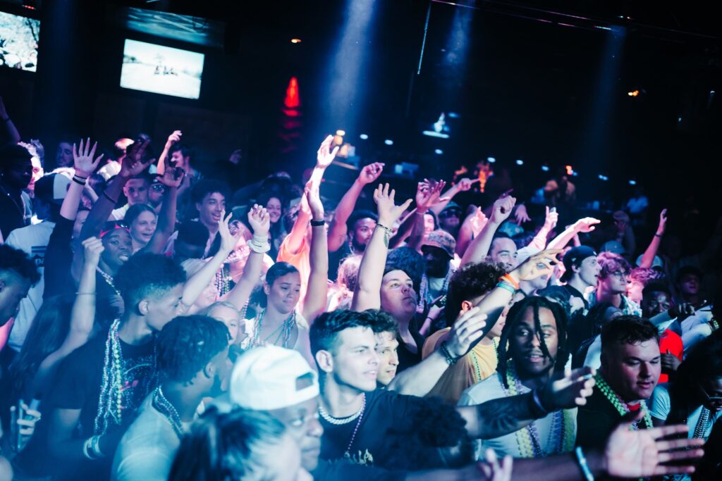 Grads in Mardi Gras beads throwing their hands up at a Senior Week Pardi Gras party