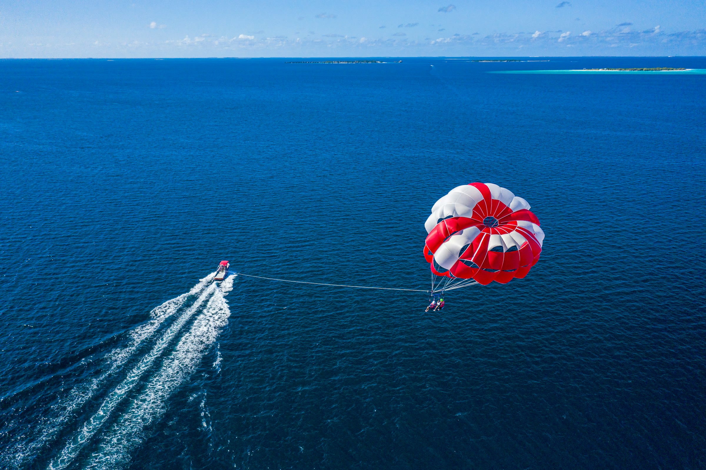 Parasailers under a red and white parachute towed by a boat over deep blue ocean